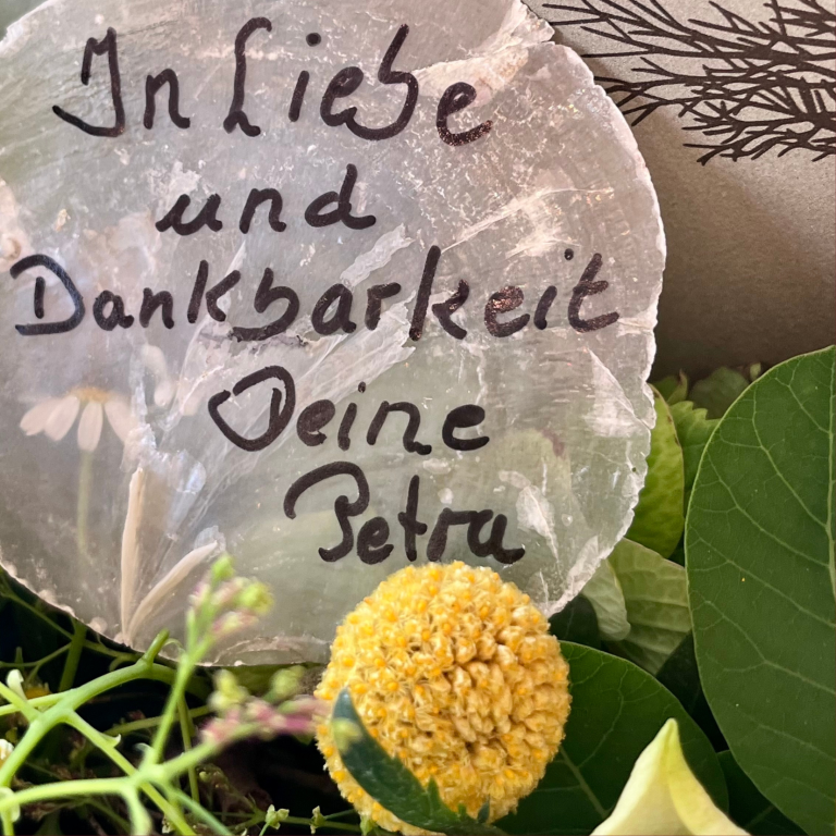 Beschriftete Muschelscheibe mit der Aufschrift: "In Liebe und Dankbarkeit, Deine Petra" im Urnenkranz statt Schleife