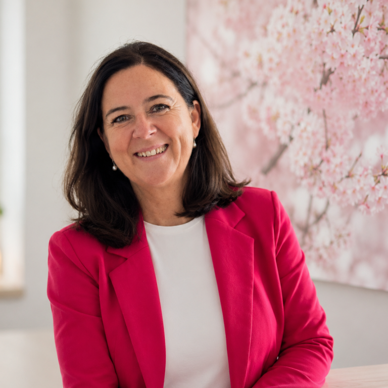 Jacqueline lächelnd vor einem Bild mit Zweigen mit Kirschblüten und dem Schriftzug auf hellem Hintergrund