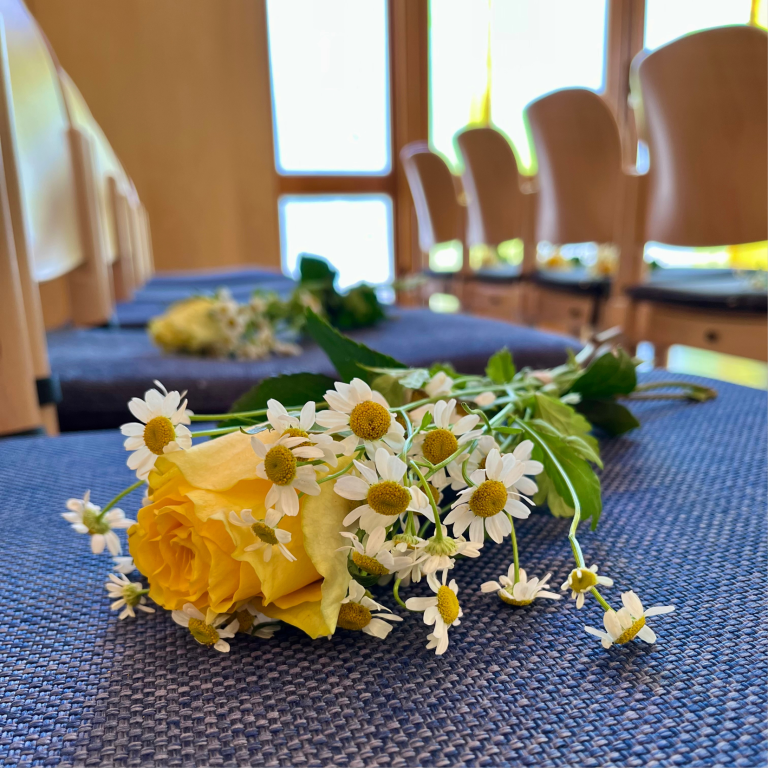 Gelbe Rosen mit weißen Blumen auf Stuhlreihen in einem hellen Raum.